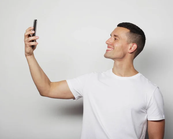 Jovem homem de camisa branca segurando telefone celular e fazendo foto de si mesmo — Fotografia de Stock