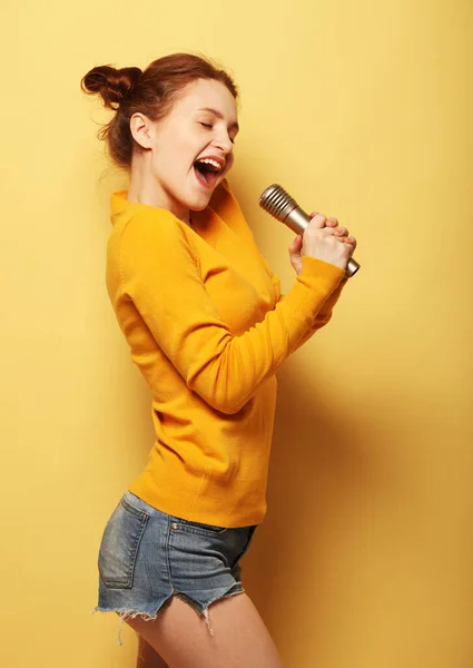 Pelirroja mujer cantando karaoke aislado sobre fondo amarillo — Foto de Stock