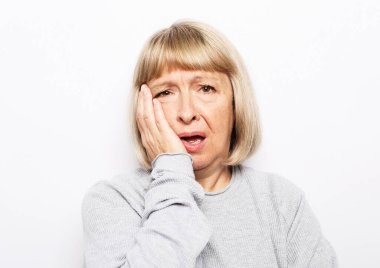 Beyaz arka planda yaşlı sarışın kadın pozu, yanağa dokunuyor.