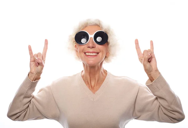 Portrait of a senior woman doing a rock symbol against a grey background — Stock Photo, Image