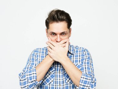 Ekose mavi gömlekli genç bir adam avuçlarıyla ağzını kapatıyor..