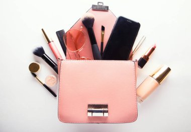 Kozmetik ve akıllı telefonlu pembe deri kadın çantası beyaz arka planda.