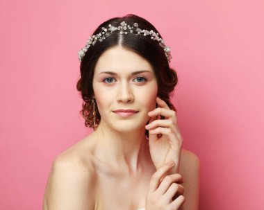 Saçlarında muhteşem diyademi olan genç gelin, pembe arka planı kapatıyor.