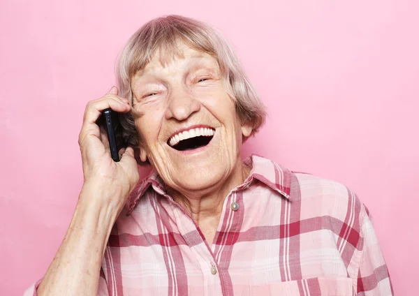 穿着休闲装、背景为粉色的手机聊天的老妇人 — 图库照片