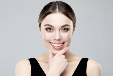 Doğal makyajlı zarif bir kadın portresi ve gri üzerinde altın dudaklar, çeneye dokunan ve kameraya bakan güzel bir kız.