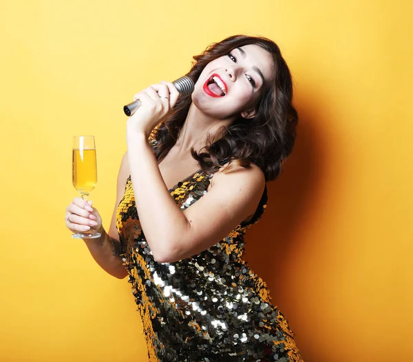 Concepto de fiesta y gente: Joven mujer de lujo con vestido de noche sosteniendo una copa de champán y micrófono. — Foto de Stock