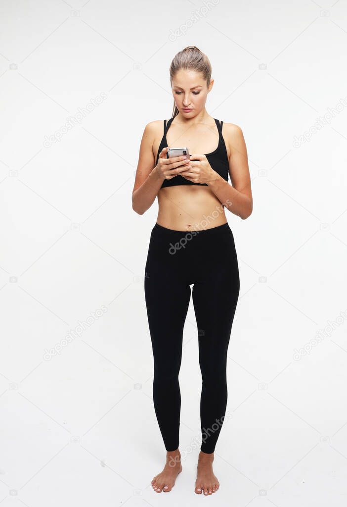 Front view of relaxed young sporty fit woman typing on cell phone. Isolated on white background.