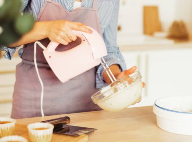 Genç bir kadın pasta için çırpıcı ve krem şanti kullanır, modern mutfakta durur.