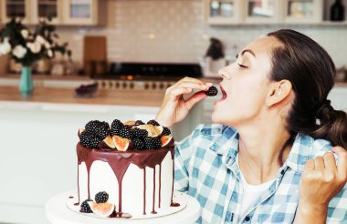 Güzel genç bir kadın pastayla çilek yiyor.
