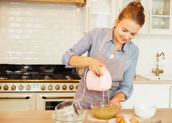 Young woman uses mixer in beating eggs, stands in a modern kitchen — Stock Photo, Image