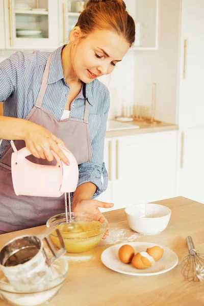Young woman uses mixer in beating eggs, stands in a modern kitchen — Stock Photo, Image