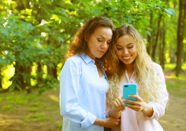 Porträt einer erwachsenen kaukasischen Tochter, die ihrer älteren Mutter in der Natur auf dem Handy zeigt — Stockfoto