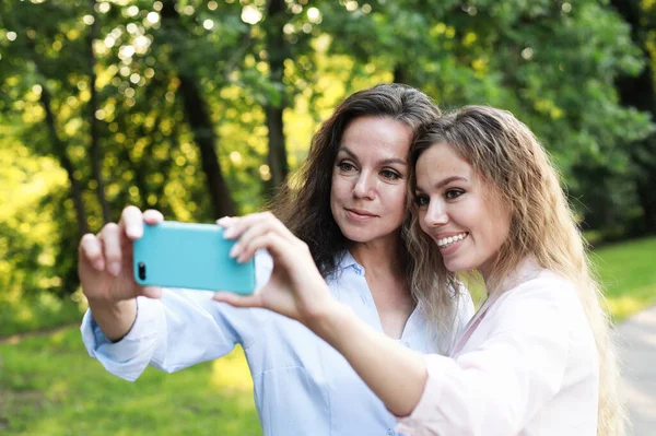 Mature mother and adult daughter are doing selfie by mobile phone in summer park — Stock Photo, Image