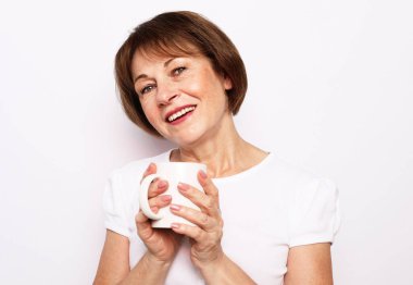 Güzel gülüşü olan neşeli yaşlı bir kadın elinde beyaz bir fincanla