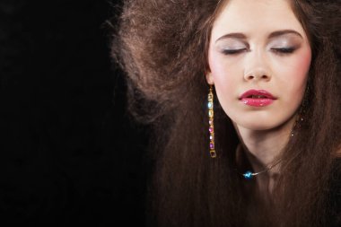 Uzun kıvırcık saçlı, akşam makyajlı, siyah elbiseli ve mücevher takan güzel bir kadın.