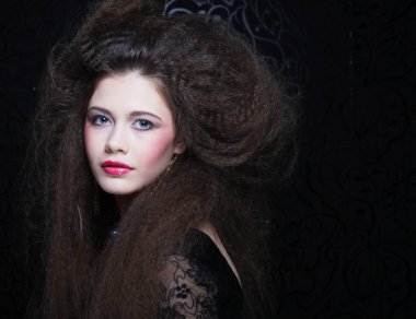 Uzun kıvırcık saçlı, akşam makyajlı, siyah elbiseli ve mücevher takan güzel bir kadın.