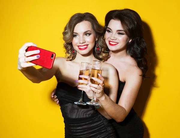 黒のカクテルドレスを着た2人のシックな若い女性がシャンパンを飲み. — ストック写真