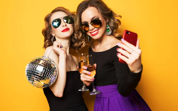 Zwei modische junge Frauen halten Discokugel in der Hand, trinken Champagner und machen ein Selfie. — Stockfoto