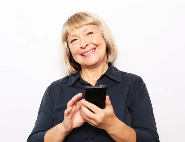 Egy idős, mosolygó hölgy portréja, amint a mobiltelefon képernyőjét nézi.. — Stock Fotó