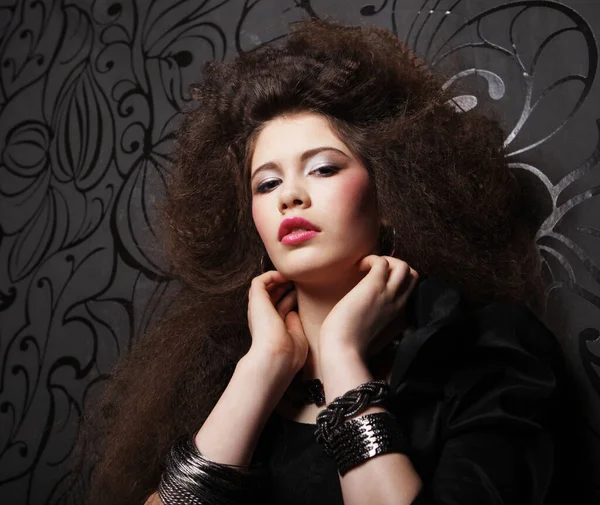 Beautiful young woman with long curly hair and evening make-up wearing black dress and jewerly — Stock Photo, Image