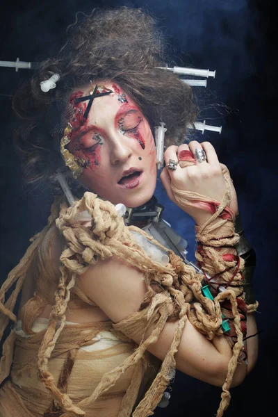 Una joven con un disfraz de zombi envuelta en vendajes y con jeringas en el pelo. Imagen creativa para la fiesta. — Foto de Stock