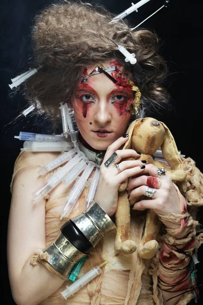 Νεαρή γυναίκα σε στυλ ζόμπι κρατώντας ένα παιχνίδι λαγουδάκι στα χέρια της, πάνω από σκοτεινό φόντο. — Φωτογραφία Αρχείου