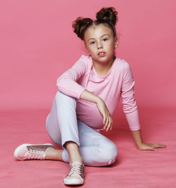 Pembe arka planda gelişigüzel poz veren tatlı küçük kız.