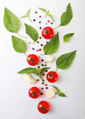 Beyaz arka planda fesleğen, biber ve sarımsaklı olgun kırmızı domatesler. Üst Manzara. Vejetaryen yemeği..