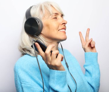 Mavi kazaklı son sınıf güzeli kulaklıklı müzik dinliyor. Beyaz arkaplan.