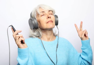 Mavi kazaklı son sınıf güzeli kulaklıklı müzik dinliyor. Beyaz arkaplan.