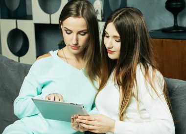 İki güzel genç bayan oturma odasında yerde dinleniyor tablete bakıyor ve ekranda bir şeye gülüyor. Yaşam tarzı, arkadaşlık, tehnoloji ve insanlar konsepti.