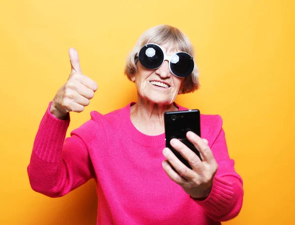 Photo of crazy ecstatic old woman wear big sunglasses use smartphone impressed social media like feedback win raise fists scream yes isolated over yelow background