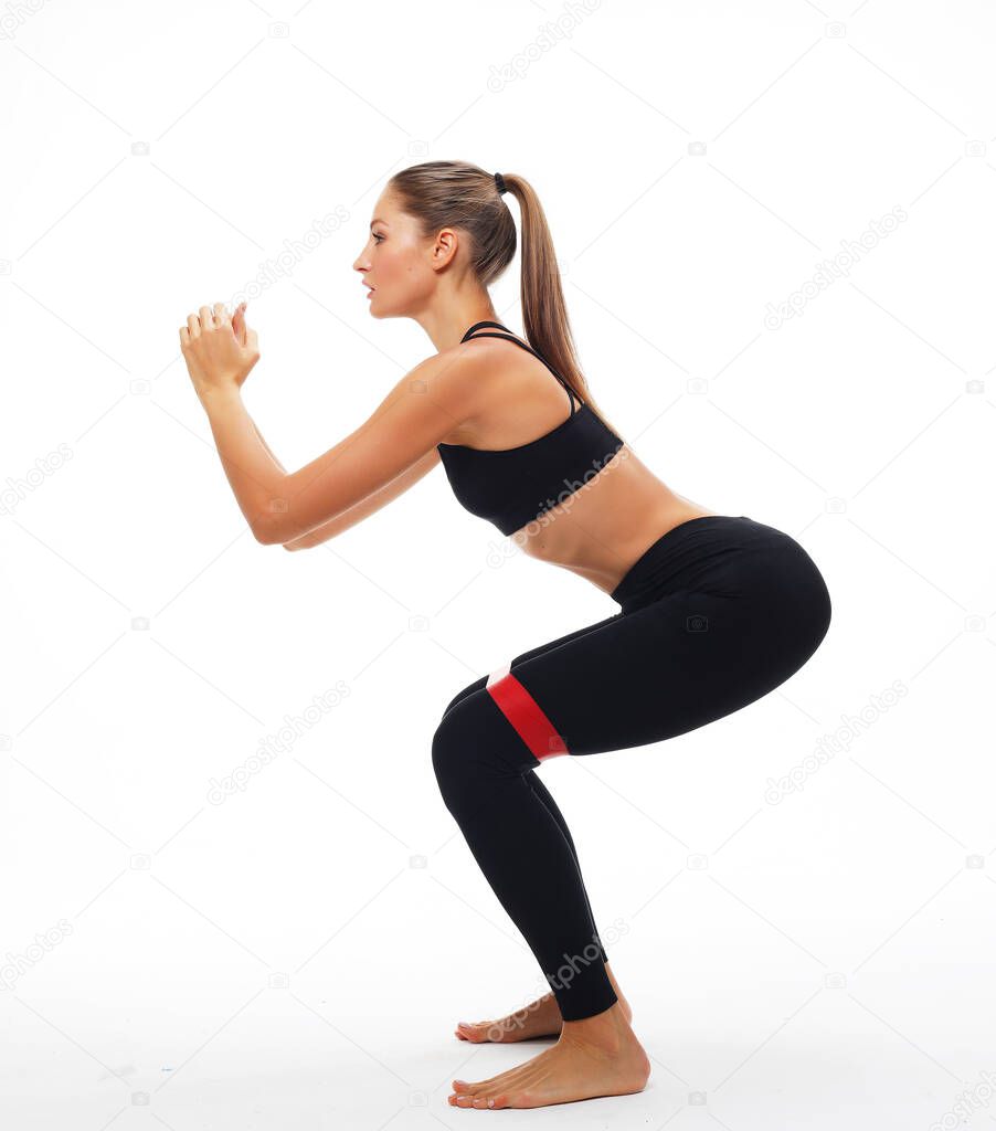 Sporty young woman squatting doing sit-ups with resistance band. Photo of woman in fashionable sportswear over white background. Strength and motivation.