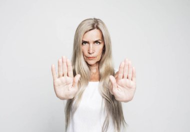 Yaşam tarzı ve duygu konsepti: Yaşlı gri saçlı kadın gri arkaplan üzerinde ciddi ve kendinden emin bir ifadeyle dur işareti yapıyor