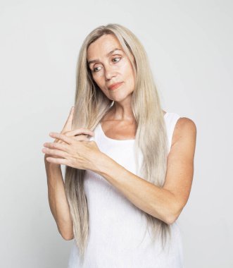 Güzellik, moda ve yaşlılar konsepti: uzun, güzel gri saçlı, saçlarını okşayan güzel yaşlı kadın, şampuan ve açık gri arka planda sağlıklı saç konsepti