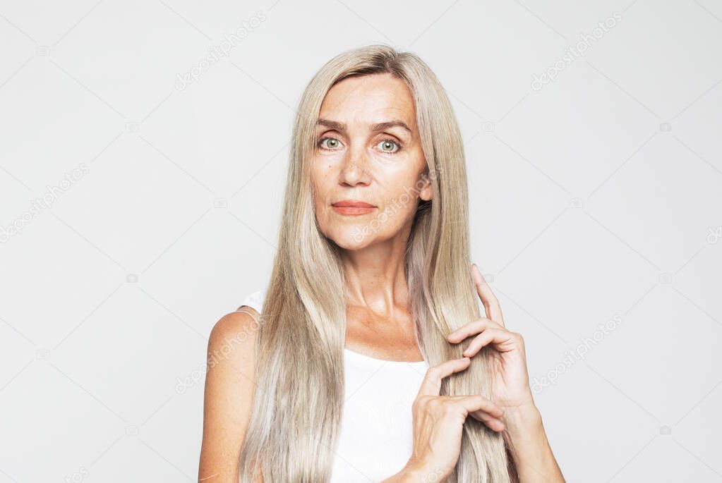 Beauty, fashion and old people concept: beautiful elderly woman with long lovely gray hair stroking her hair, shampoo and healthy hair concept over light grey background