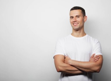 Yaşam tarzı, duygu ve insan konsepti: yakışıklı genç adam gri arka planda kameraya bakarken beyaz tişört giyiyor