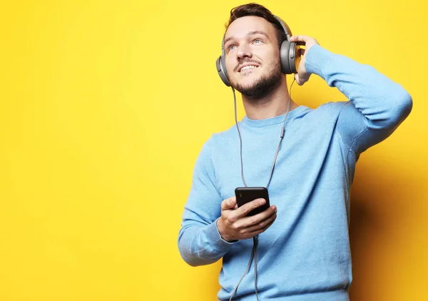 生活方式与人的概念 身穿蓝色毛衣 头戴耳机 背景为黄色 手持手机的年轻人 — 图库照片