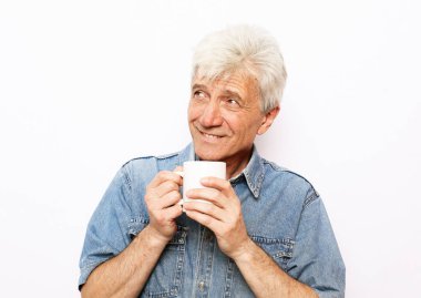 Bir fincan kahve tutan ve beyaz arka planda gülümseyen yaşlı, neşeli bir adam. Yaşam tarzı kavramı.