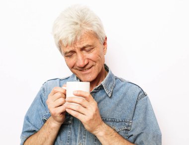 Bir fincan kahve tutan ve beyaz arka planda gülümseyen yaşlı, neşeli bir adam. Yaşam tarzı kavramı.