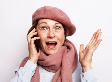 Pembe fularlı, bereli ve telefonda konuşan neşeli, başarılı yaşlı kadın. Olumlu duygular. Yaşam tarzı konsepti. Beyaz arkaplanı kapat.