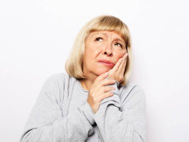 Stüdyo resmi. Yaşlı, sarışın, gri arka planda poz veren, aniden diş ağrısı çeken yanaklara dokunan, sağlıksız, mutsuz, dişçi yardımı, tıbbi sigorta konsepti.