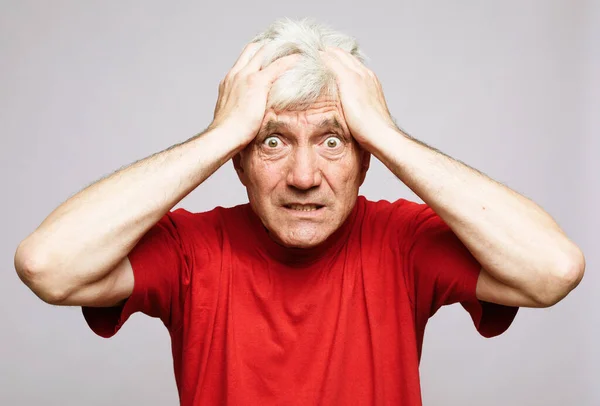Portrait of anxious senior man in red t-shirtholding his head. I\'m afraid that I will be exposed and someone will know my terrible secret emotion