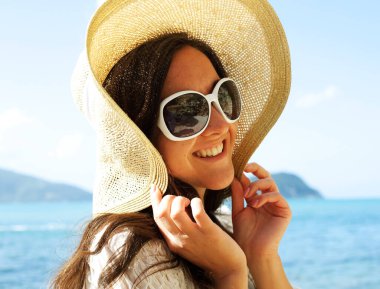 Yaşam tarzı ve insan konsepti: Büyük şapka ve güneş gözlüğü takan mutlu kadın yaz mevsimi, okyanus kenarında