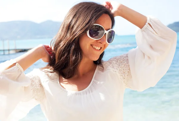快乐的黑发女人穿着夏天的白衣 戴着太阳镜在海滩上 白种人女性在度假时放松并享受和平 — 图库照片