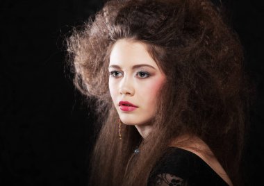 Uzun kıvırcık saçlı, akşam makyajlı, siyah elbiseli ve mücevher takan güzel bir kadın.