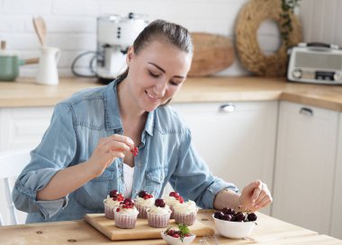 Yaşam tarzı, yemek pişirme ve serbest çalışma konsepti: Genç kadın pasta şefi çörekleri böğürtlenlerle süslüyor