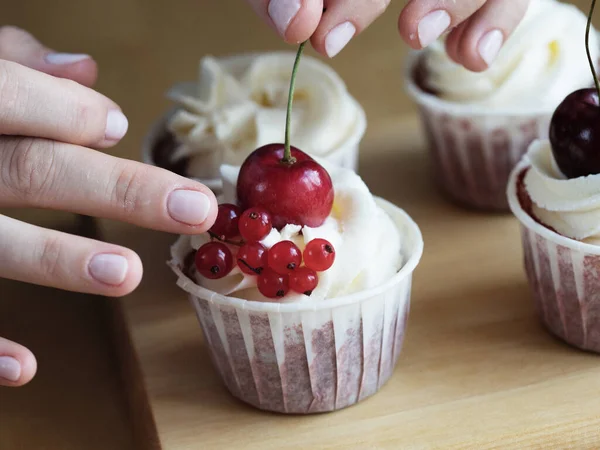 Lifestyle, cooking and freelance concept: hands close-up of young woman pastry chef decorates cupcakes with berries
