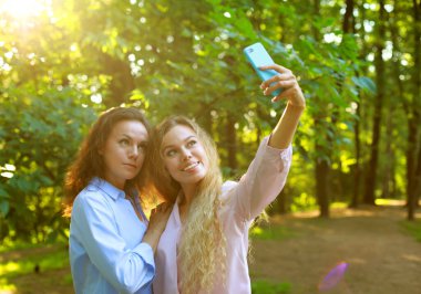 Yaşam tarzı, duygu, aile ve insan kavramı: olgun anne ve yetişkin kız yaz parkında cep telefonuyla selfie çekiyor