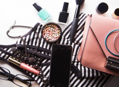 Kozmetik ürünleri, aksesuarlar ve beyaz arka planda akıllı telefonlu pembe deri kadın çantası.